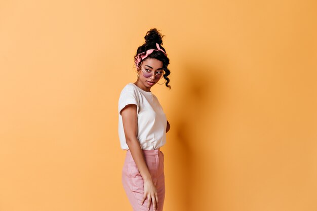 Femme pensive à lunettes debout sur le mur jaune