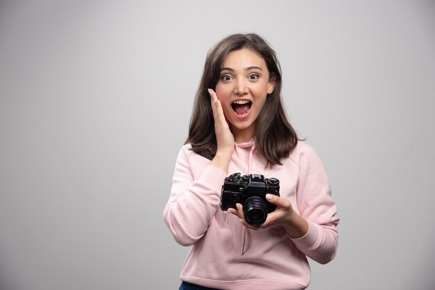 Femme photographe posant avec appareil photo sur mur gris.