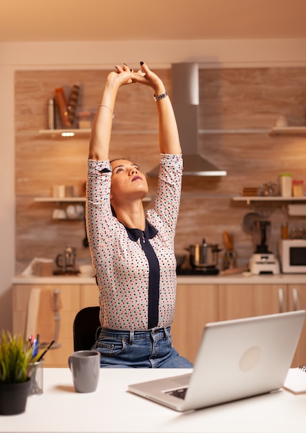 Femme pigiste épuisée s'étirant tout en travaillant sur une date limite tard dans la nuit. Employé utilisant la technologie moderne à minuit faisant des heures supplémentaires pour le travail, les affaires, occupé, carrière, réseau, style de vie, sans fil