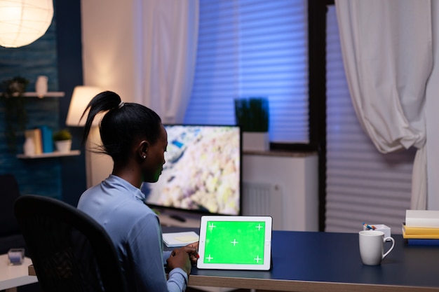 Femme pigiste noire travaillant à domicile tard dans la nuit avec un appareil disposant d'un espace de copie disponible assis au bureau. Utilisation d'un ordinateur d'affichage à clé chroma de maquette.