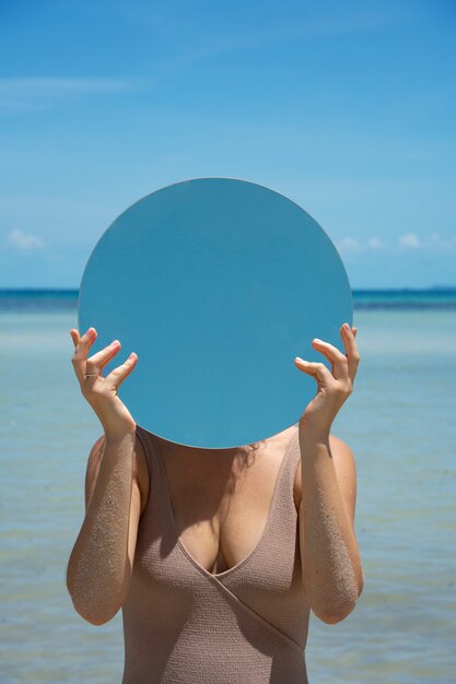 Femme à la plage en été posant avec miroir rond