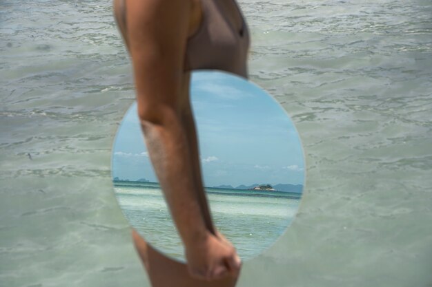 Femme à la plage en été posant avec miroir rond