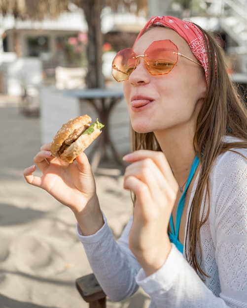 Femme sur la plage, manger un hamburger