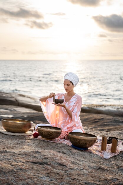 Femme plein coup avec des bols chantants au bord de la mer