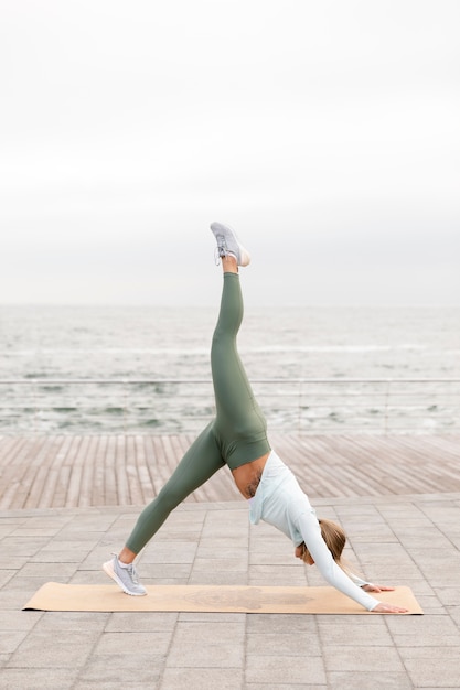 Femme pleine de coups faisant du yoga au bord de la mer