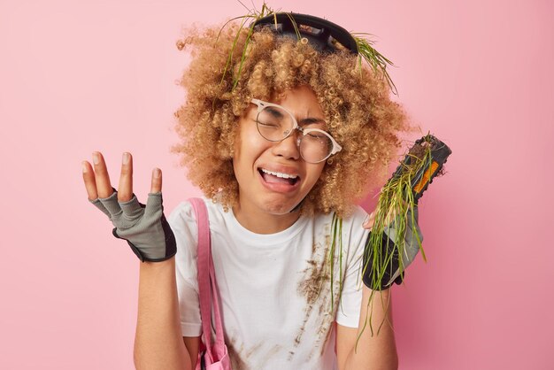 Une femme en pleurs bouleversée s'arrête en chemin à cause d'une panne de vélo porte des vêtements sales a une expression désespérée porte des gants de protection isolés sur fond rose Émotions négatives et style de vie actif