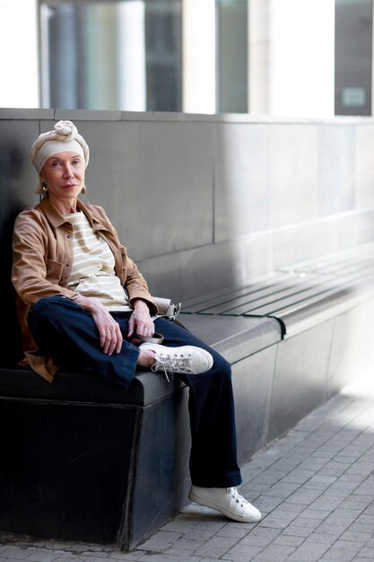 Femme plus âgée à l'extérieur de la ville assise sur un banc