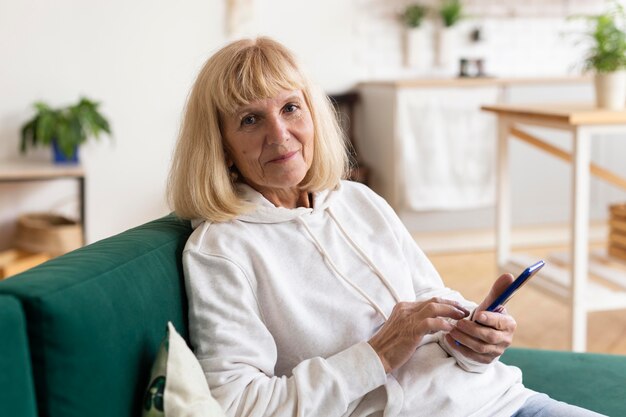 Femme plus âgée à la maison sur le canapé à l'aide d'un smartphone