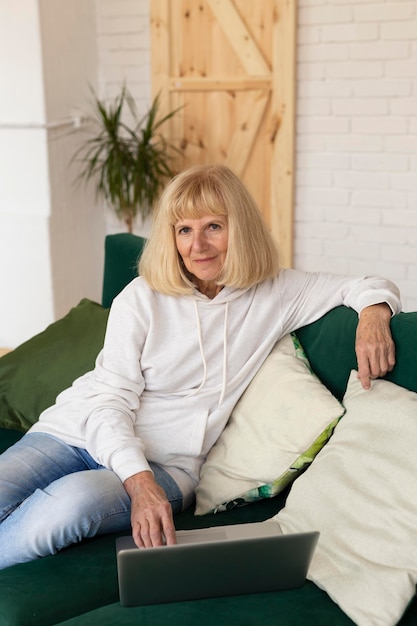 Femme plus âgée à la maison sur le canapé avec ordinateur portable