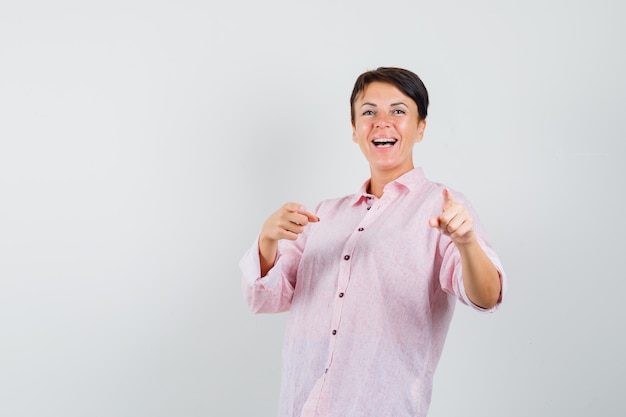 Femme pointant la caméra en chemise rose et à la vue de face, fringante.