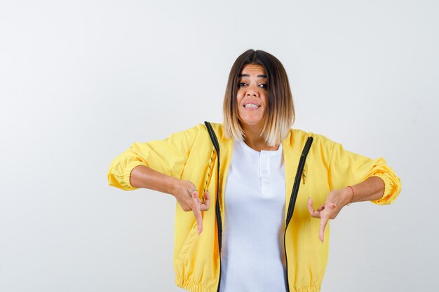 Femme pointant vers le bas en t-shirt, veste et à la curieuse. vue de face.