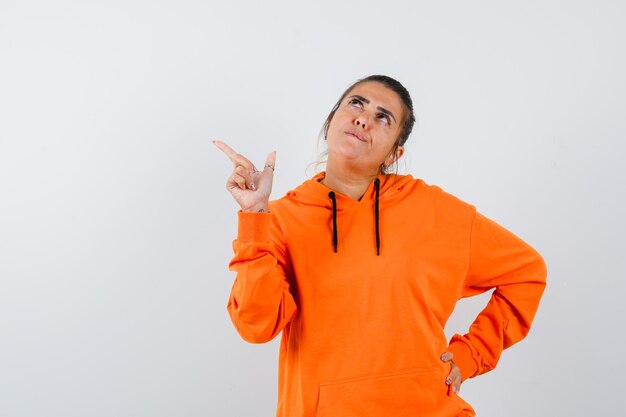 femme pointant vers le coin supérieur gauche en sweat à capuche orange et à la pensive