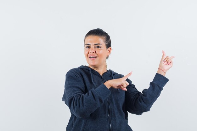 Femme pointant vers le côté droit en sweat à capuche et ayant l'air confiante. vue de face.