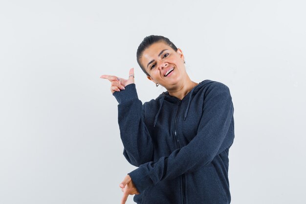 Femme pointant vers le côté gauche en sweat à capuche et ayant l'air confiante. vue de face.