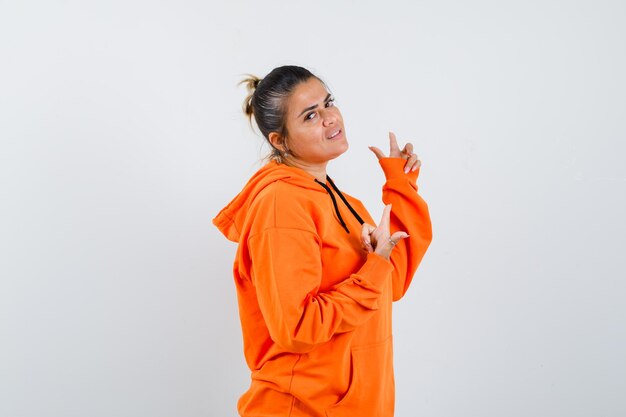 Femme pointant vers le haut dans un sweat à capuche orange et ayant l'air confiant. .