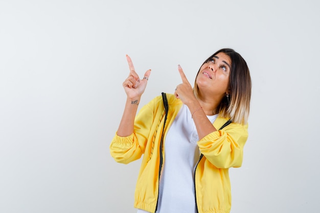 Femme pointant vers le haut en t-shirt, veste et à la recherche focalisée, vue de face.