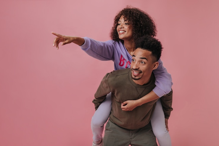 Photo gratuit une femme pointe vers la gauche alors qu'elle est assise sur le dos de son petit ami