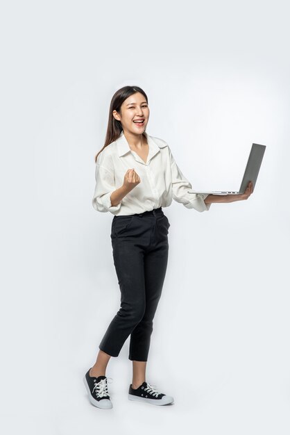 La femme portait une chemise blanche et un pantalon sombre, tenant un ordinateur portable et faisant semblant d'être joyeuse