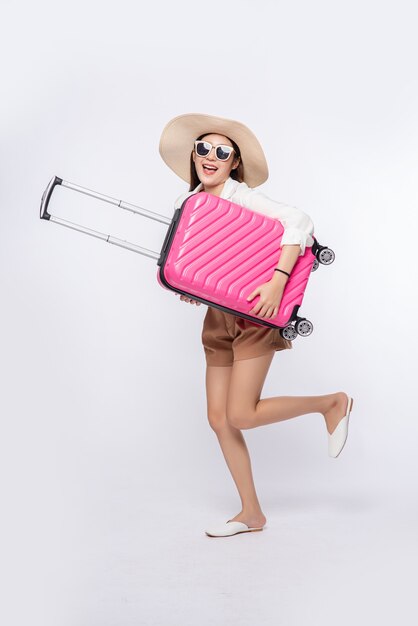 Femme portant un chapeau, des lunettes et des poignées de valises pour voyager