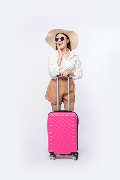 Femme portant un chapeau, des lunettes et des poignées de valises pour voyager