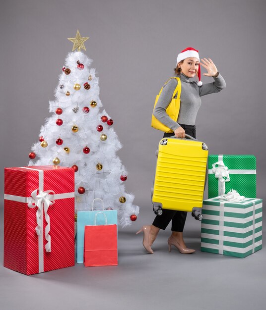 Femme portant un chapeau de père Noël avec des bagages à côté de l'arbre de Noël