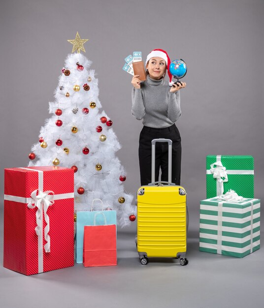 Femme portant un chapeau de père Noël avec des bagages à côté de l'arbre de Noël