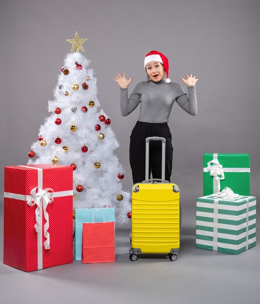 Femme portant un chapeau de père Noël avec des bagages à côté de l'arbre de Noël