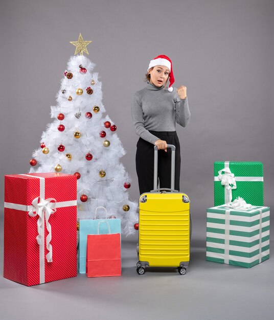 Femme portant un chapeau de père Noël avec des bagages à côté de l'arbre de Noël