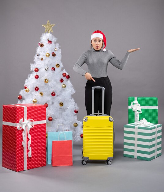 Femme portant un chapeau de père Noël avec des bagages à côté de l'arbre de Noël