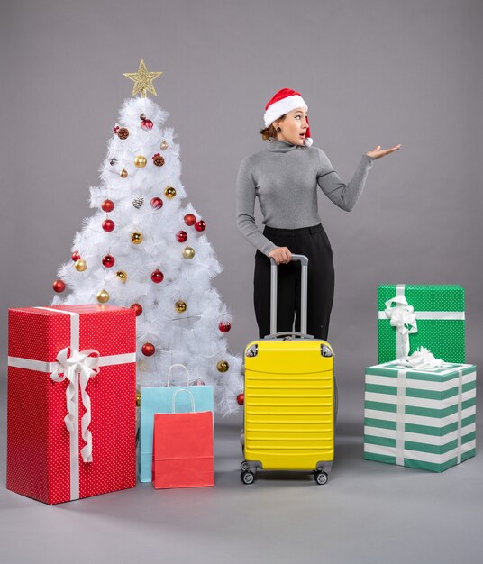 Femme portant un chapeau de père Noël avec des bagages à côté de l'arbre de Noël