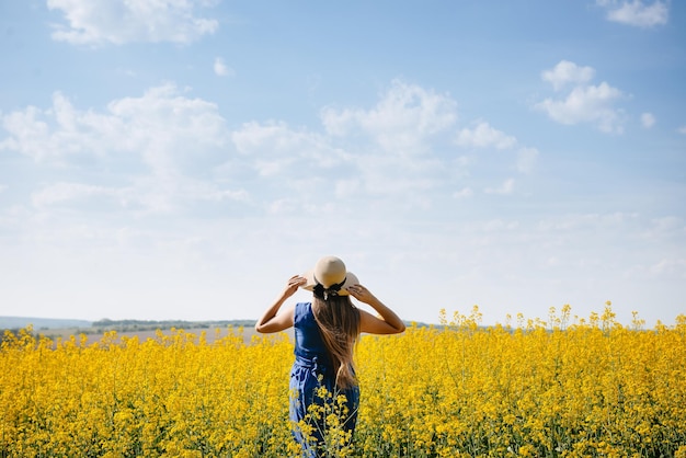 Femme portant un chapeau se tient à l'extérieur dans un champ d'été jaune avec ciel bleu et nuages