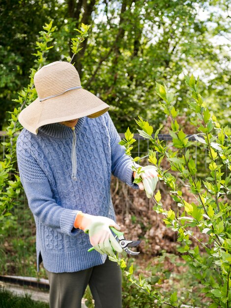 Femme portant un chapeau tout en coupant les feuilles de son jardin