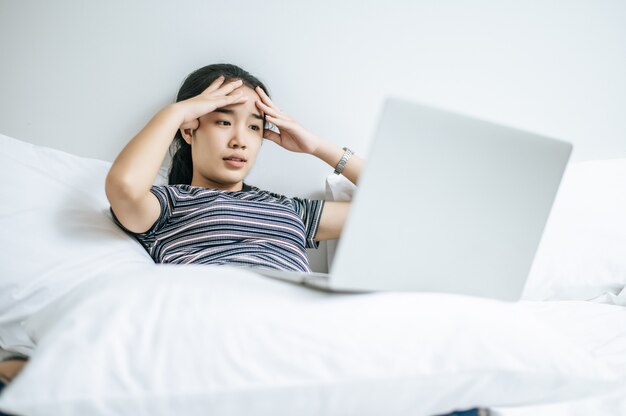 Une femme portant une chemise rayée sur le lit et jouant un ordinateur portable.
