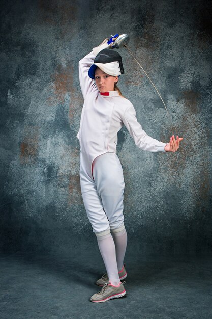 La femme portant un costume d'escrime avec une épée contre le gris