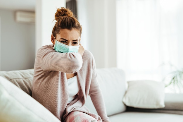 Photo gratuite femme portant des éternuements dans son coude tout en portant un masque protecteur à la maison