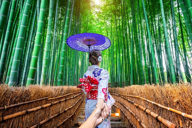 Femme portant un kimono traditionnel japonais tenant la main de l'homme et le menant à la forêt de bambous à Kyoto, au Japon.