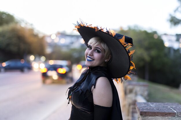 Femme portant un maquillage et un costume de sorcière avec un chapeau décoré capturé dans une rue