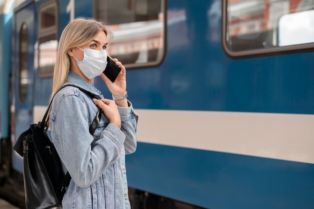 Photo gratuite femme portant un masque médical et parlant au téléphone tout en se préparant à voyager en train