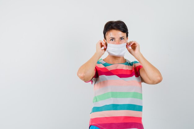 Femme portant un masque médical en t-shirt rayé et regardant prudemment.