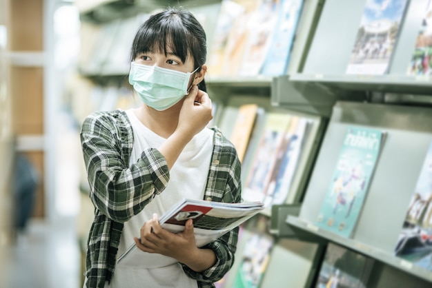 Une femme portant un masque et à la recherche de livres dans la bibliothèque.
