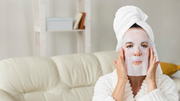 Femme portant un peignoir et appliquant un masque facial