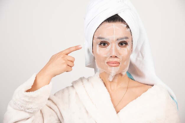 Femme portant un peignoir et une serviette avec masque facial.