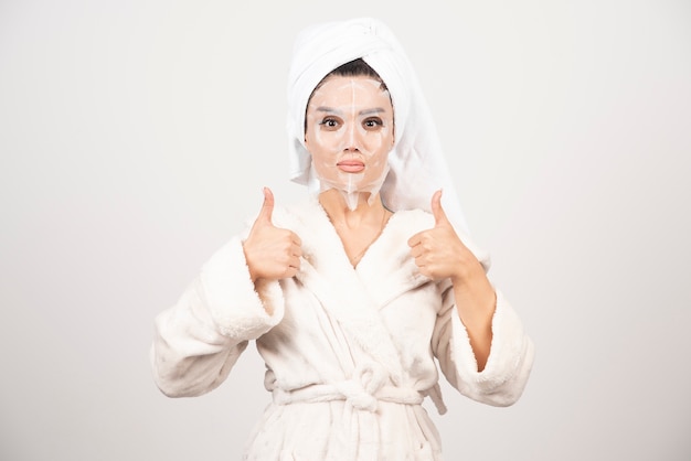 Femme portant un peignoir et une serviette avec masque facial.