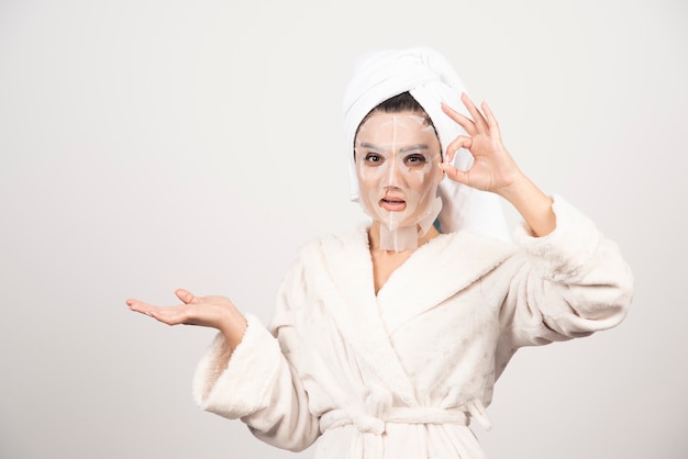 Femme portant un peignoir et une serviette avec masque facial.