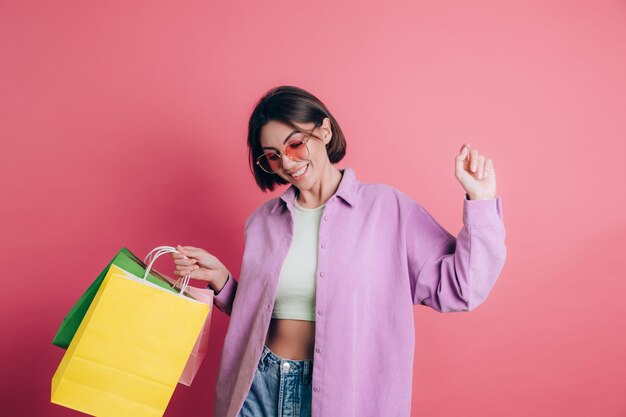 Femme portant un pull décontracté sur fond heureux de profiter du shopping tenant des sacs colorés portant des lunettes de soleil d'été