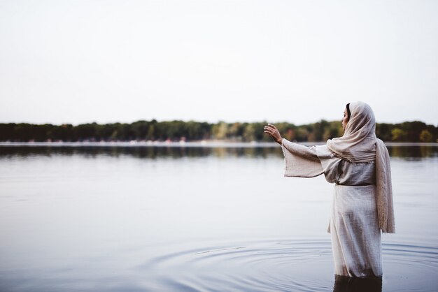 Femme portant une robe biblique et debout dans l'eau avec sa main