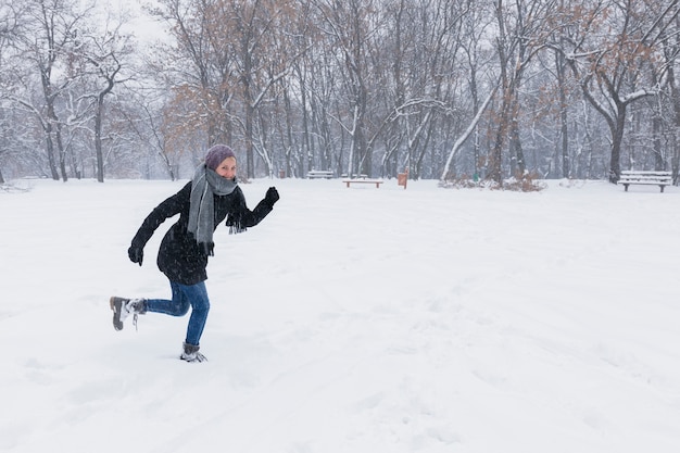 Femme portant des vêtements chauds en cours d&#39;exécution sur un terrain enneigé en hiver
