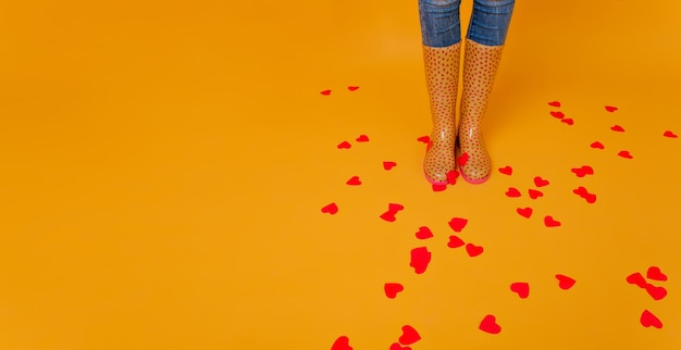 Photo gratuite femme porte des bottes en caoutchouc debout sur le revêtement de sol avec de nombreux cœurs. photo de studio d'une femme galbée en gommes jaunes posant pour la saint-valentin.