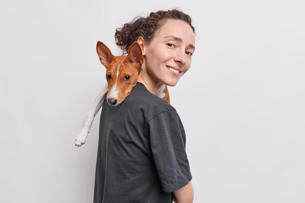 une femme porte un chien sur l'épaule joue avec son animal de compagnie préféré exprime l'amour et les soins se tient sur le côté isolé sur blanc