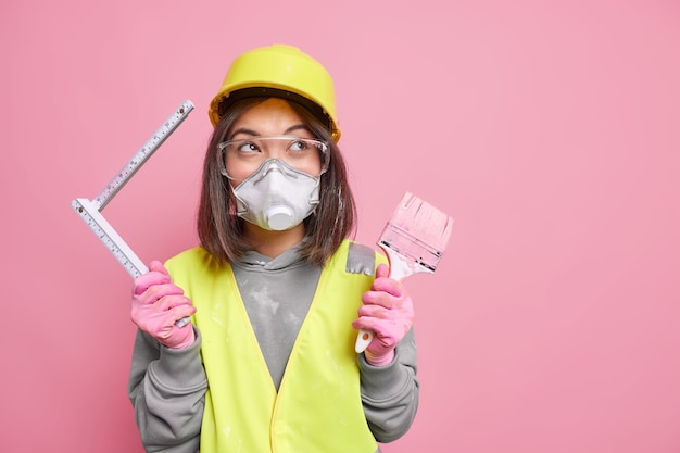 Une Femme Porte Des Lunettes De Sécurité, Un Respirateur Et Un Casque, Tient Un Pinceau à Peinture, Un Ruban à Mesurer, Des Réparations